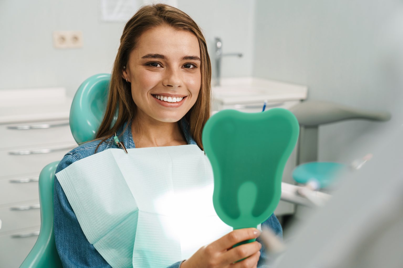 european young woman smiling while looking at mirror in dental c